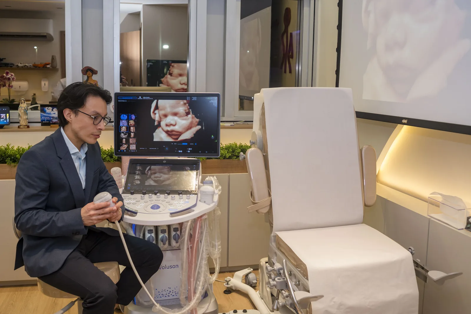 Dr. Héctor sentado ao lado da maca de exame, segurando o transdutor do aparelho de ultrassom